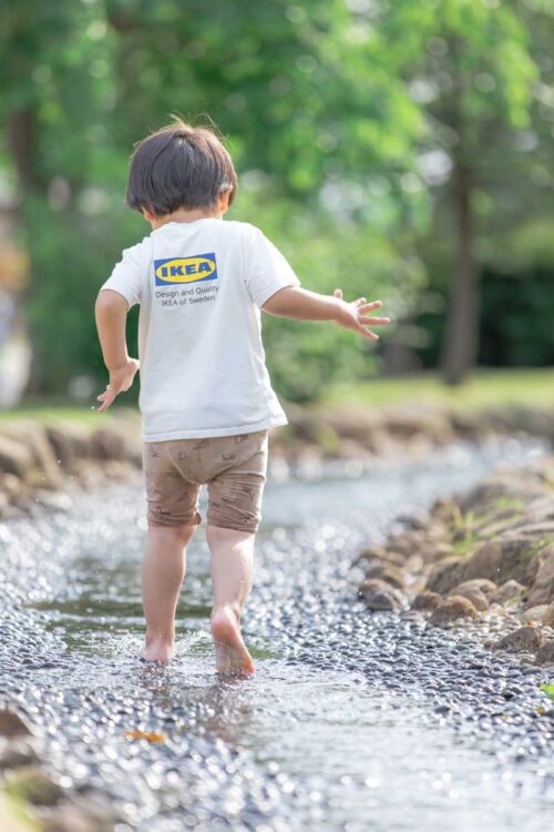 小川で水しぶきをあげ走る子供の写真